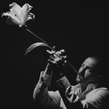 Avishai Cohen, sur fond noir, utilisant une fleur de lys blanche comme trompette