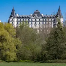 Façade d'un hôtel vue de loin, derrière de la végétation dense, semblable à un château avec ses tours latérales symétriques et son belvédère central