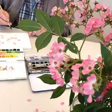 Sur une table, en premier plan à droite, un bouquet de rose sert de modèle à un peintre aquarelliste