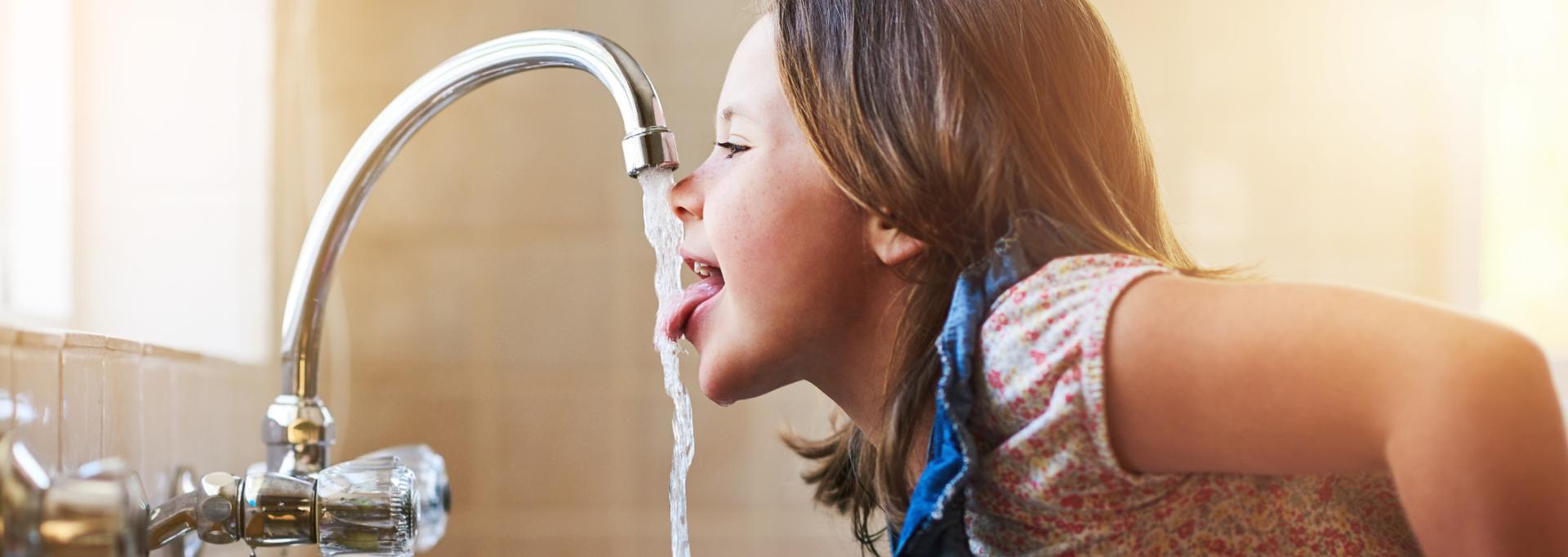 Une enfant en train de boire de l'eau au robinet 