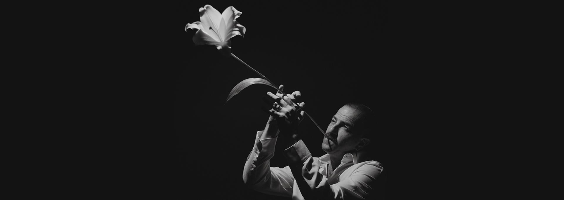 Avishai Cohen, sur fond noir, utilisant une fleur de lys blanche comme trompette