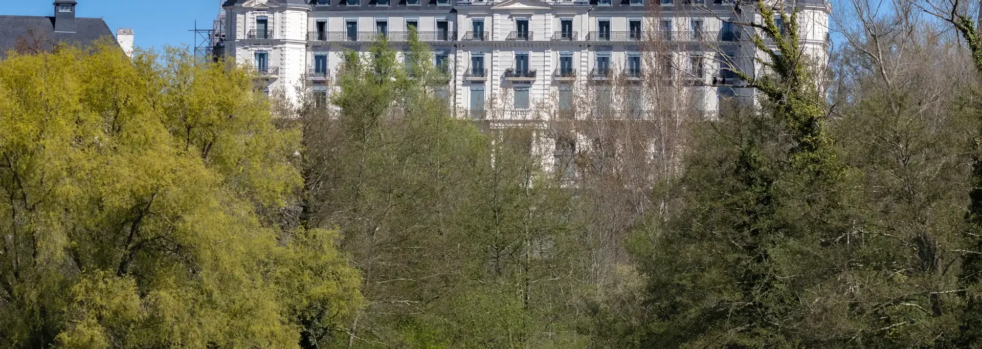 Façade d'un hôtel vue de loin, derrière de la végétation dense, semblable à un château avec ses tours latérales symétriques et son belvédère central