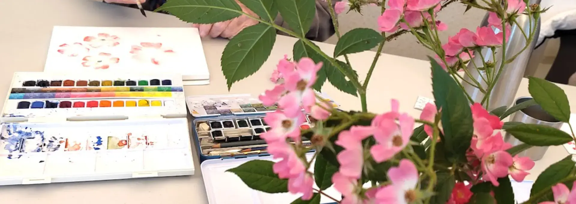 Sur une table, en premier plan à droite, un bouquet de rose sert de modèle à un peintre aquarelliste