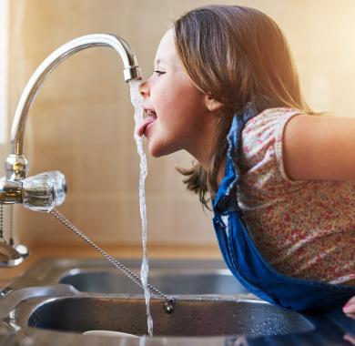 Une enfant en train de boire de l'eau au robinet 