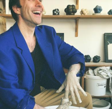 Thomas Poitevin sourit assis devant un tour de poterie qu'il modèle