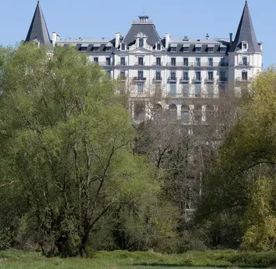 Façade d'un hôtel vue de loin, derrière de la végétation dense, semblable à un château avec ses tours latérales symétriques et son belvédère central