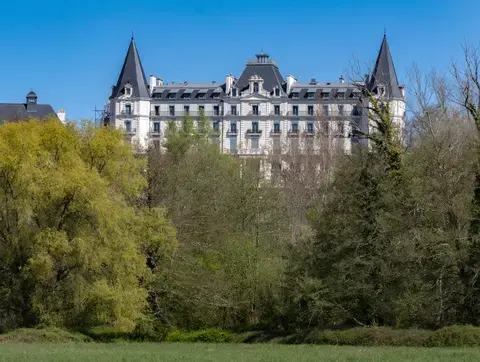 Façade d'un hôtel vue de loin, derrière de la végétation dense, semblable à un château avec ses tours latérales symétriques et son belvédère central