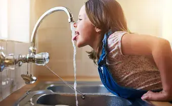 Une enfant en train de boire de l'eau au robinet 