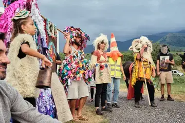 Un groupe d'adultes et d'enfants avec costumes de laine et sonnailles effectuent une transhumance artistique en Vallée d'Aspe.